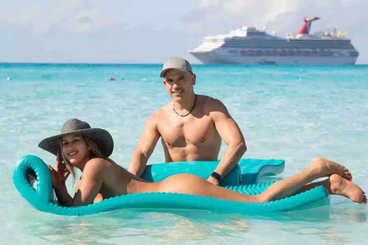 Imatge d'una parella nudista a la platja amb el creuer nudista de fons
