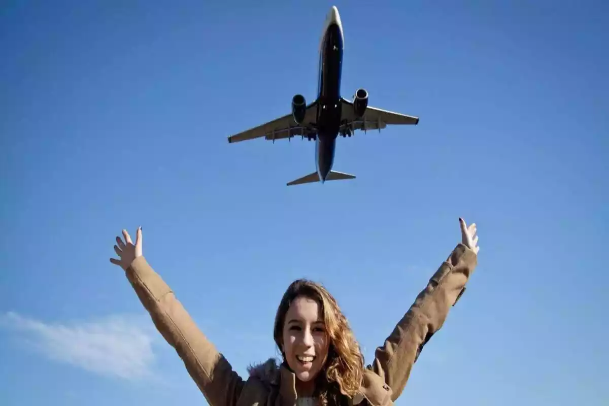 Una noia aixeca els braços i somriu mentre passa un avió per sobre