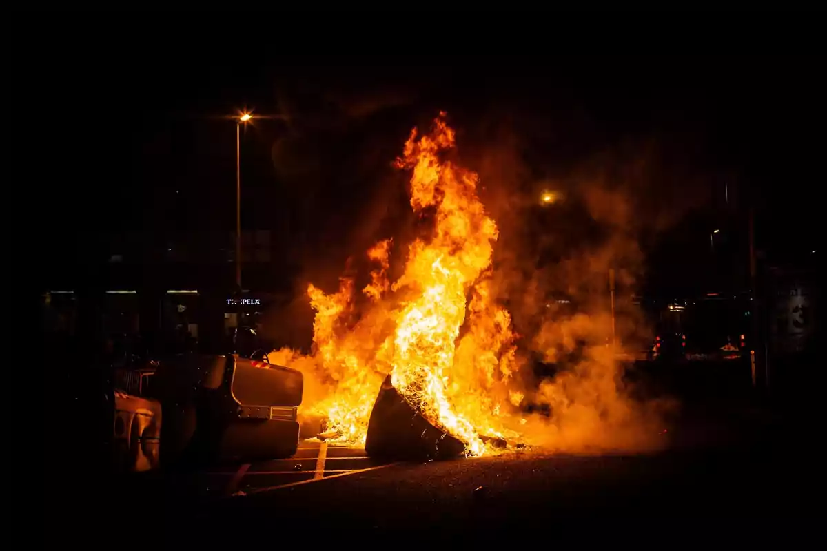 Un cotxe en flames en un carrer durant la nit.