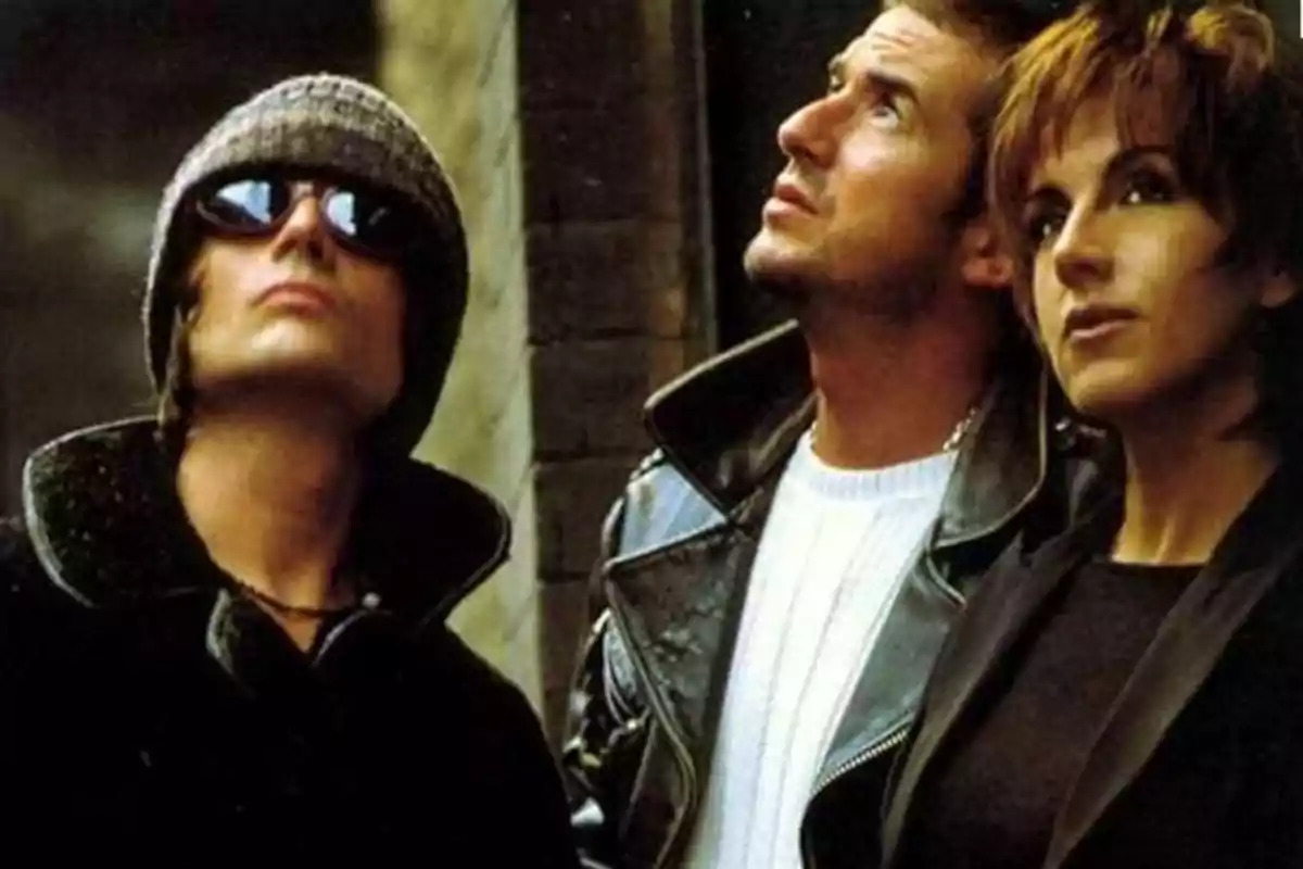 Tres persones mirant cap amunt, una porta ulleres de sol i gorra, una altra porta una jaqueta de cuir i la tercera té els cabells curts.