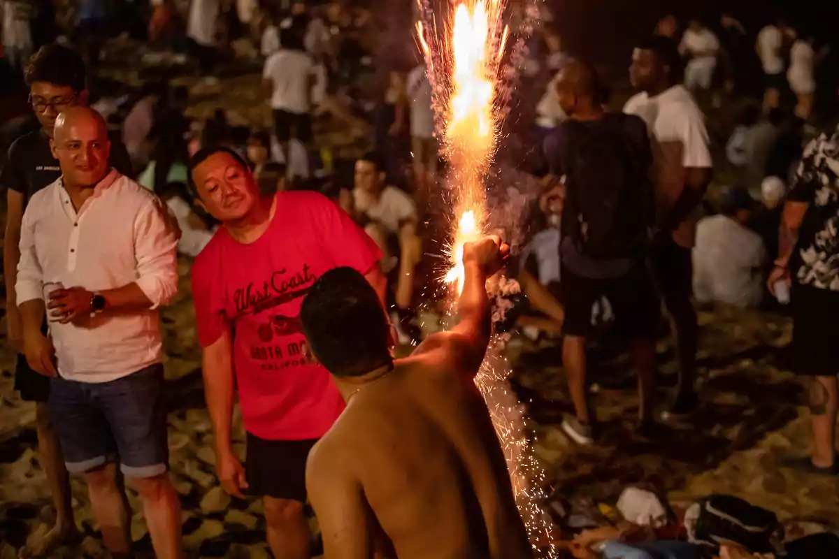 Persones gaudint d´una festa nocturna a la platja amb focs artificials.