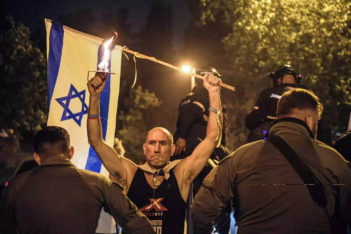 Un manifestant sosté la bandera d'Israel i una torxa amb una barrera policial al voltant de la residència del primer ministre Netanyahu