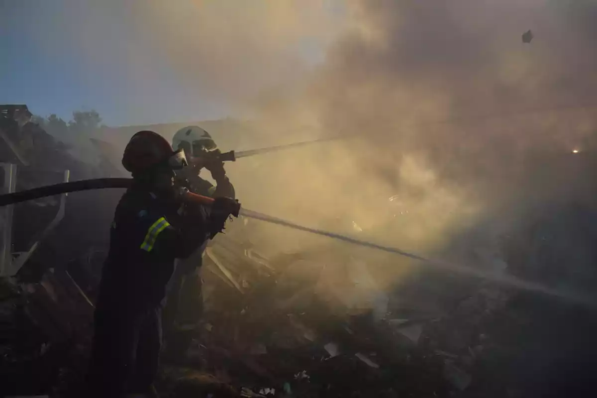 Bombers combatent un incendi enmig de runes i fum dens.