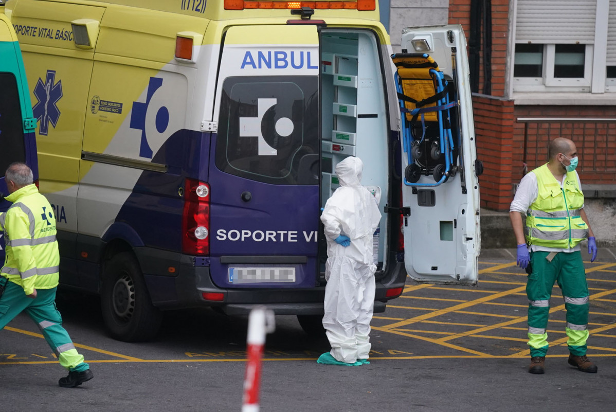 Diversos sanitaris protegits, un amb un vestit i un altre amb mascareta i guants de làtex, al costat d'una ambulància a l'Hospital Universitari Creus, un dels hospitals públics bascos de referenc