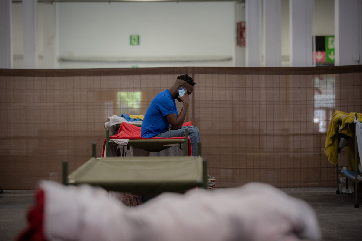 Un home consulta el seu mòbil al seu llit a l'interior de les instal·lacions de l'alberg de Fira Barcelona, habilitat per la crisi de la pandèmia de l'coronavirus per 225 persones sense sostre. A Barcelona, Catalunya (España), a 28 de maig de 2020.