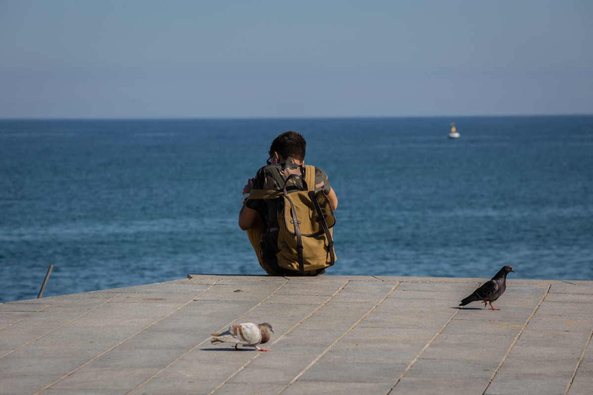 Un jove assegut al Passeig Marítim de la Platja de la Barceloneta.