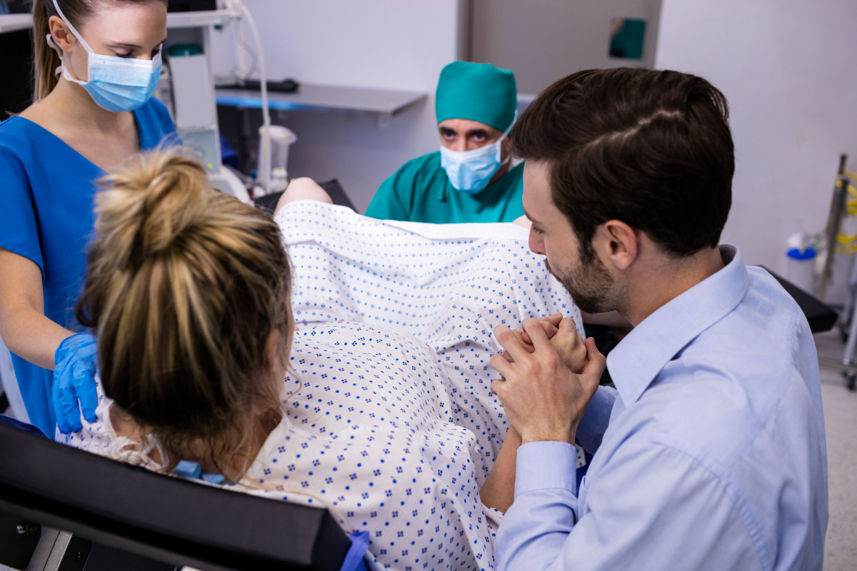 Equip mèdic examina dona embarassada part mentre que home sosté la mà